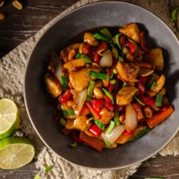 Kung Pao chicken with peanuts, red peppers, and green onions in a gray bowl with chopsticks.