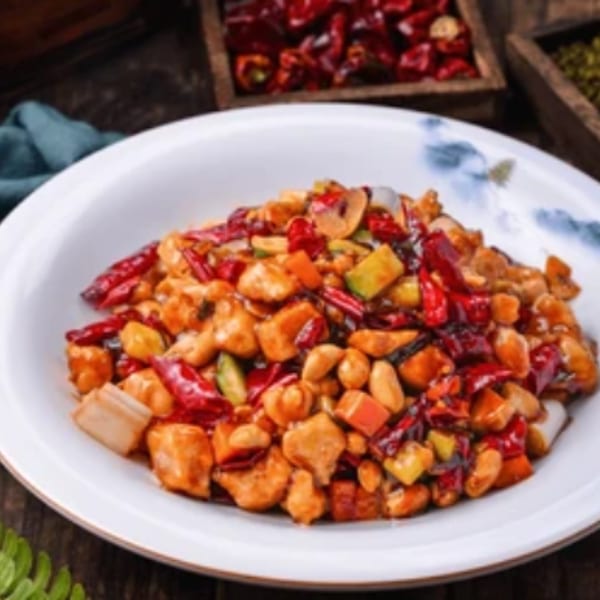 Spicy Kung Pao chicken with peanuts, red chilies, and vegetables in a white bowl.