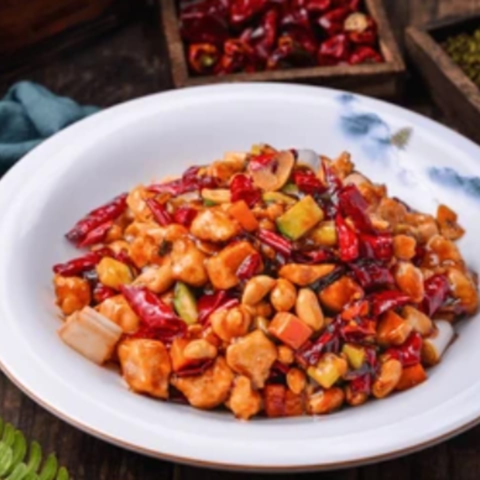 Spicy Kung Pao chicken with peanuts, red chilies, and vegetables in a white bowl.